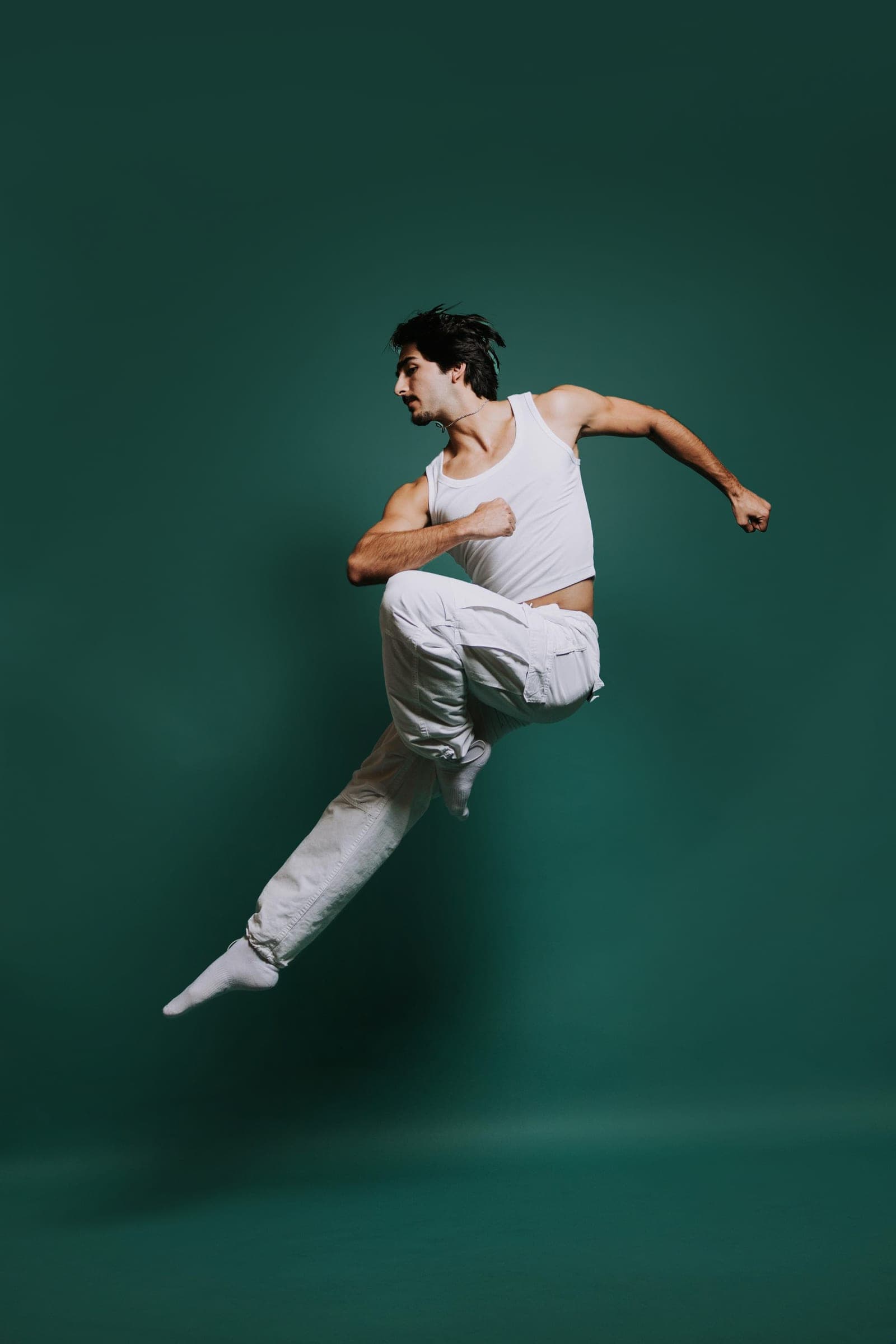 Reid Salvador mid-jump, knee driven up and arms cocked, against a deep green studio backdrop