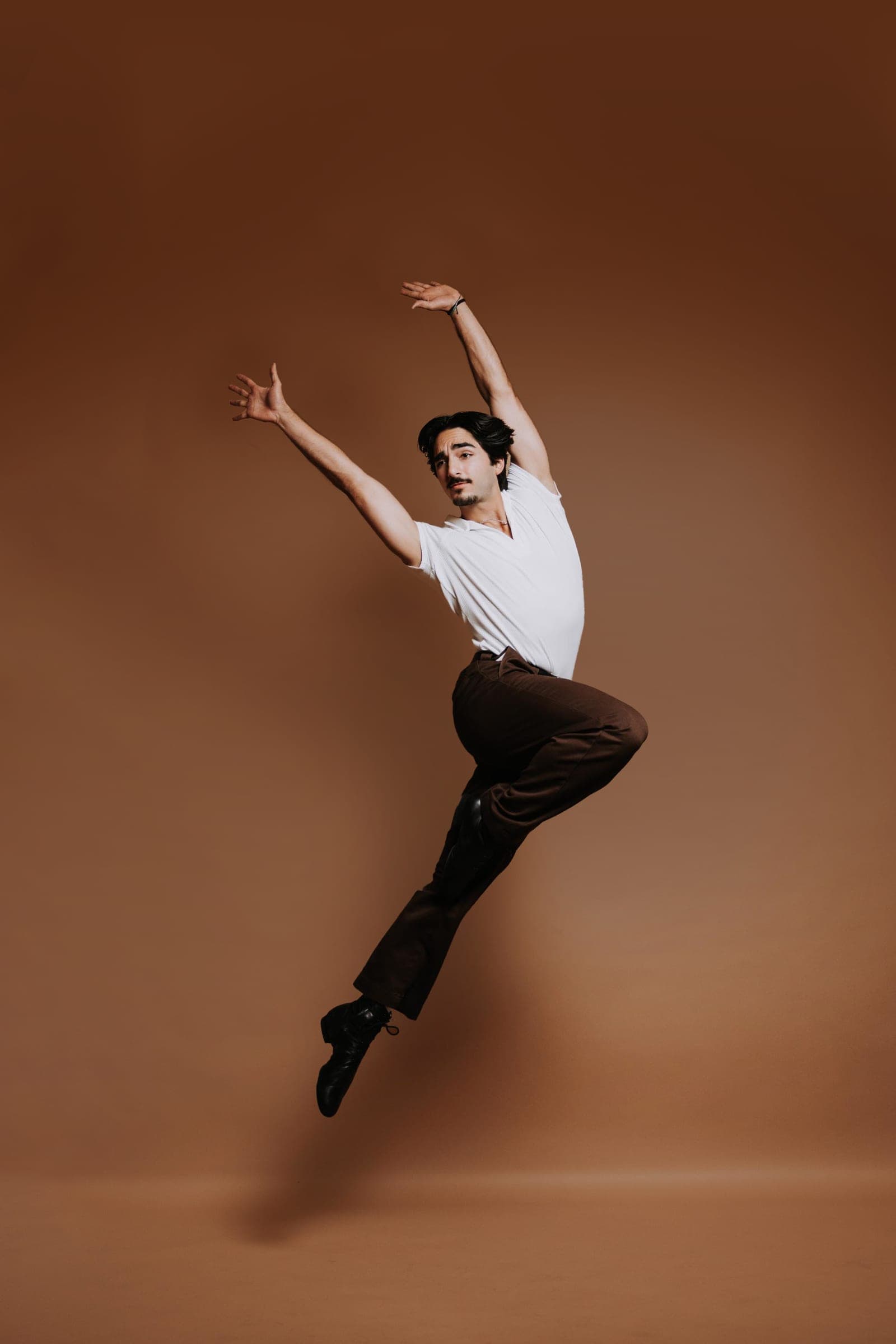 Reid Salvador airborne with both arms swept overhead against a warm terracotta studio backdrop