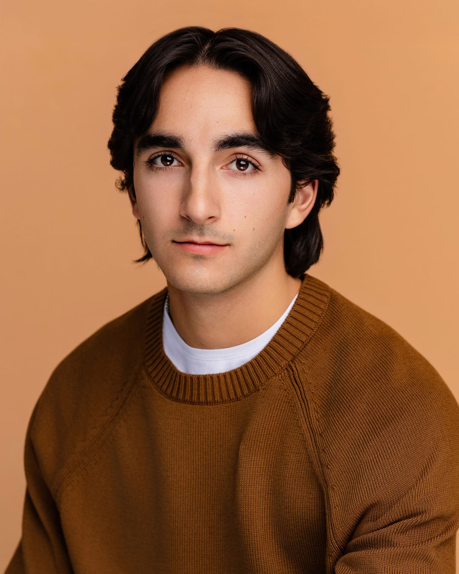Reid Salvador headshot in a rust knit sweater against a warm tan backdrop