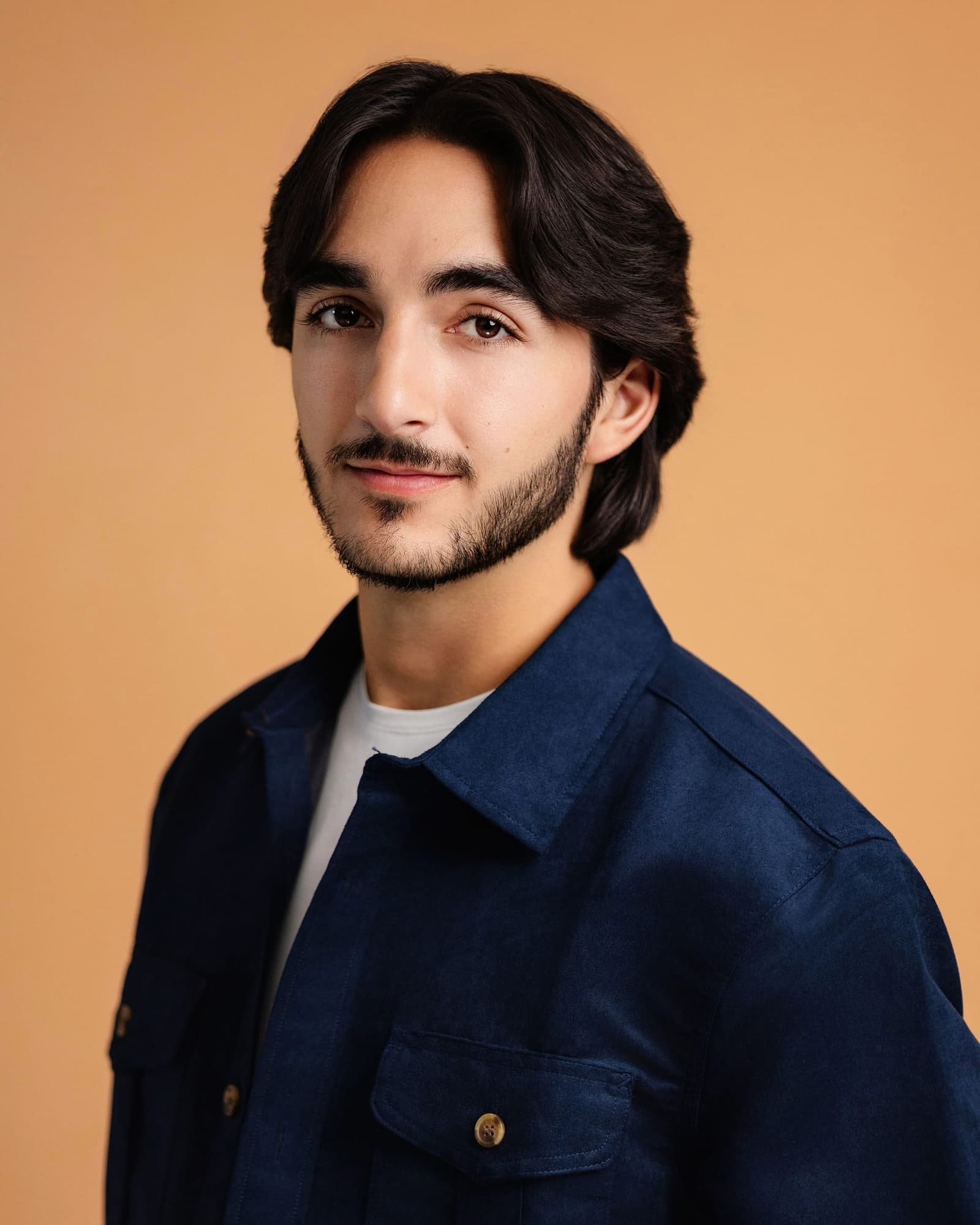 Reid Salvador headshot in a navy overshirt, turned three-quarters, against a warm tan backdrop